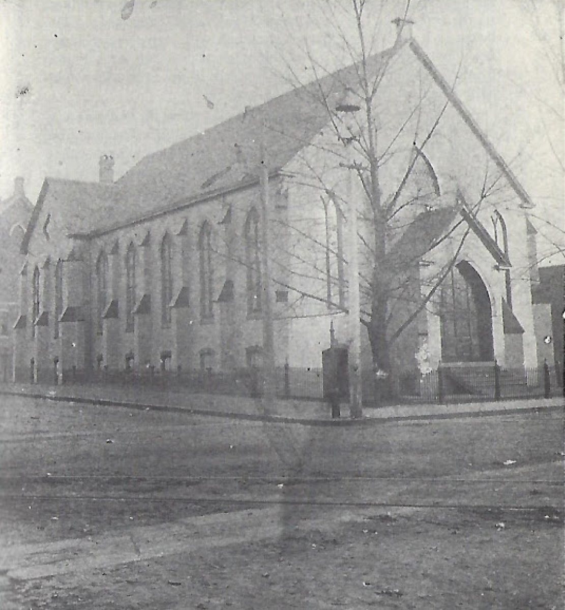 An old black and white photograph of a stone church on a street corner, with bare trees